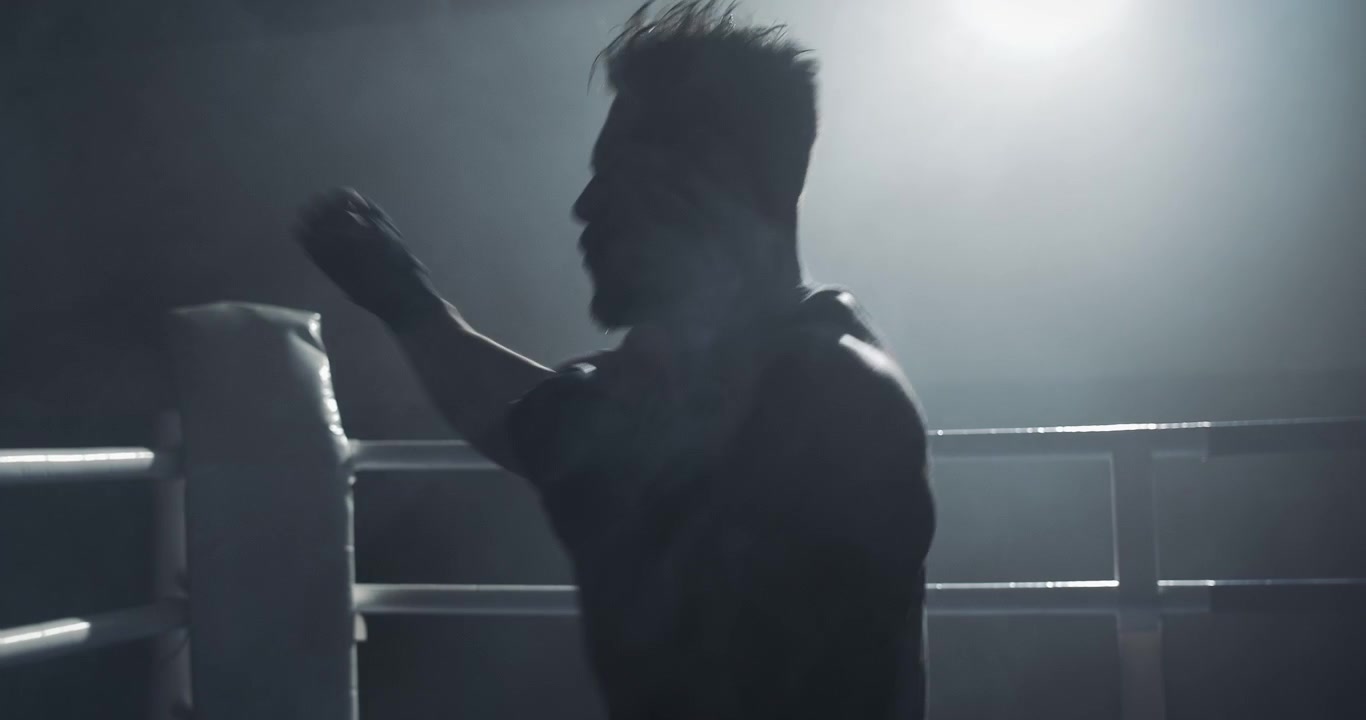 Silhouette di un pugile che fa shadow boxing in un ring buio.