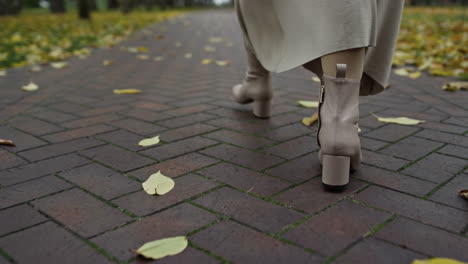 woman legs in boots walking along path in autumn park