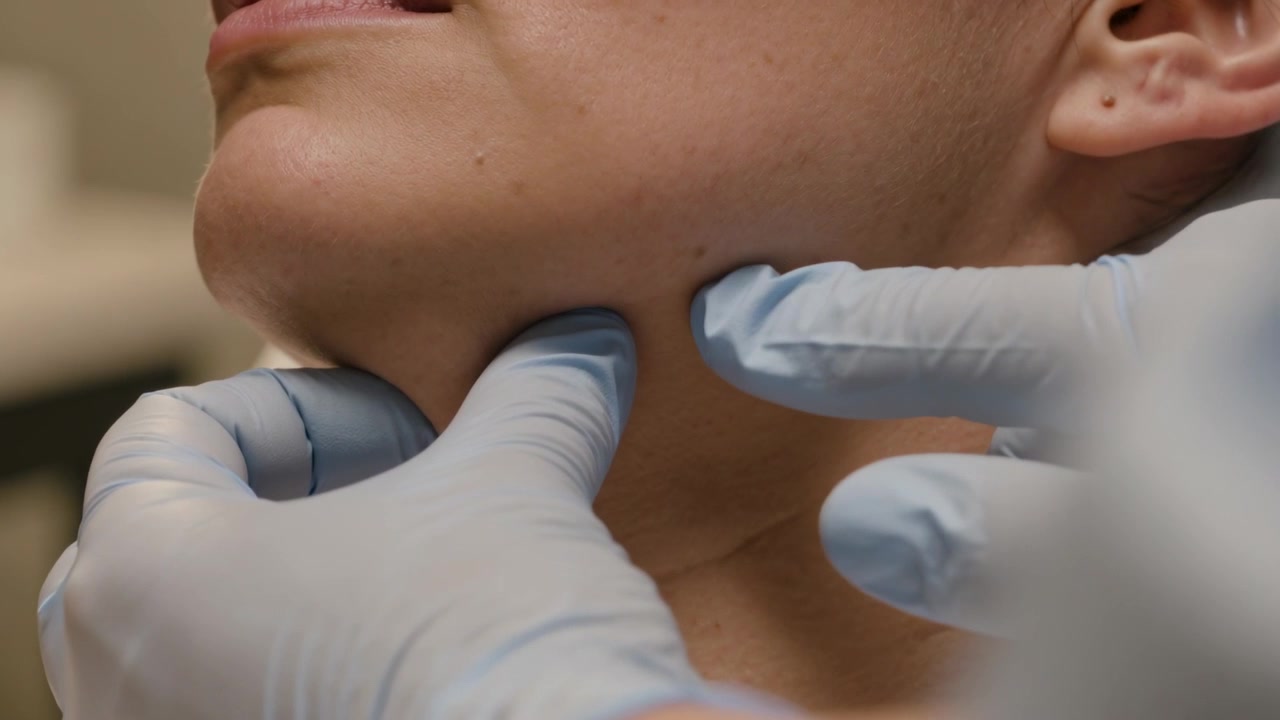 Clinico con guanti blu che, dopo aver reclinato il paziente, ne palpa la mascella e il collo durante l'esame, controllando la presenza di noduli
