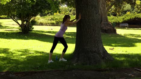 corredora estirando las piernas apoyándose contra un árbol