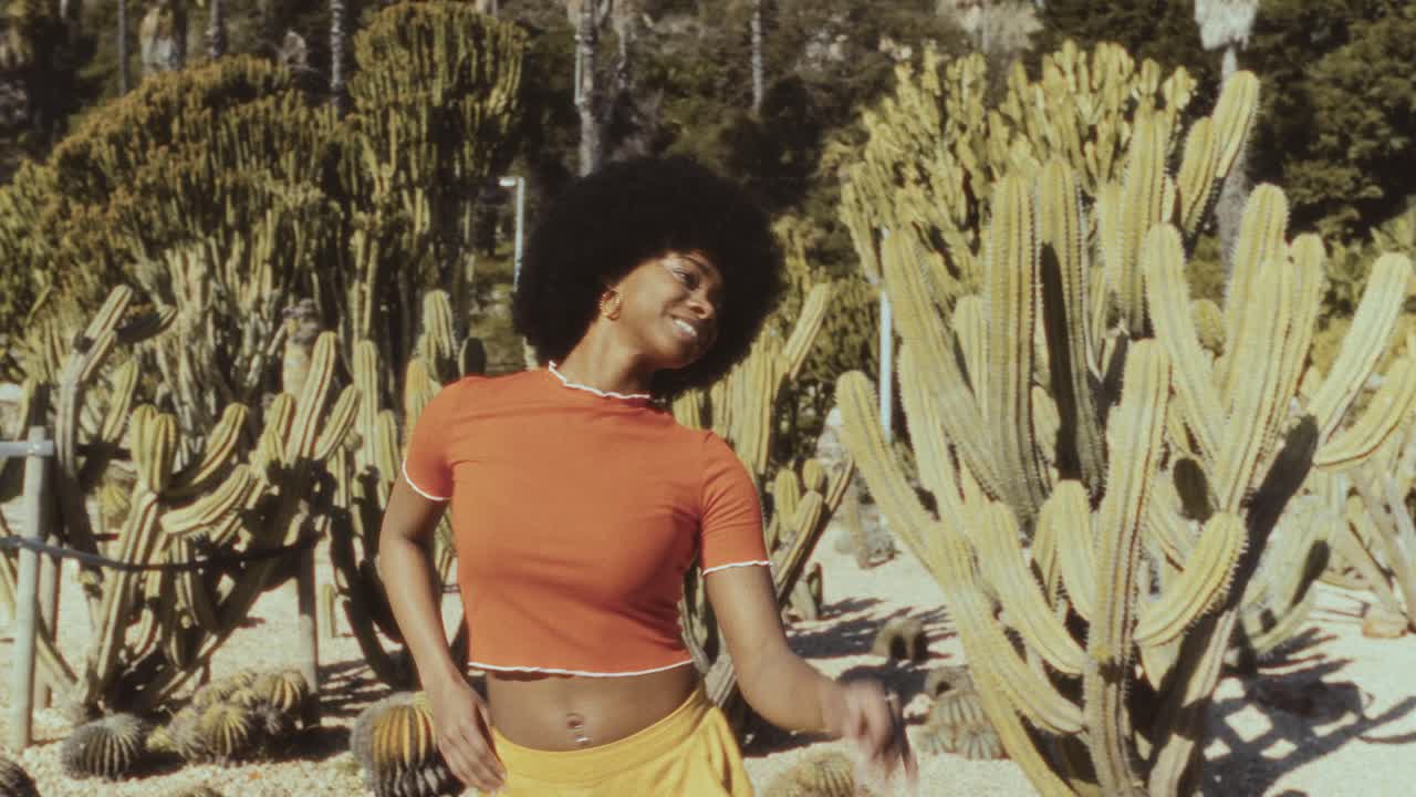 Giovane donna di colore felice con afro che balla in un giardino di cactus