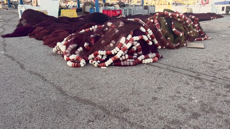 Pila di reti da pesca e attrezzatura, grande pila giacente su superficie asfaltata all'aperto in un magazzino, concetto di industria della pesca