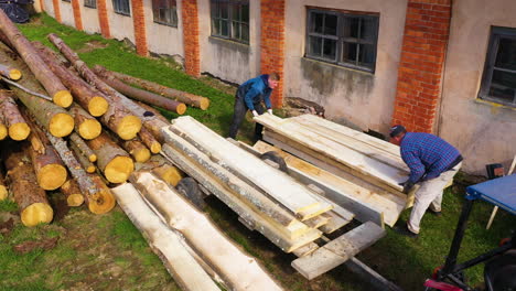 two workers stacking lumber in pile outdoors next to sawmill for drying in sun