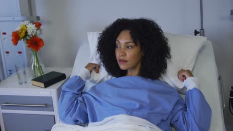 mixed race woman lying in hospital bed fluffing her pillow