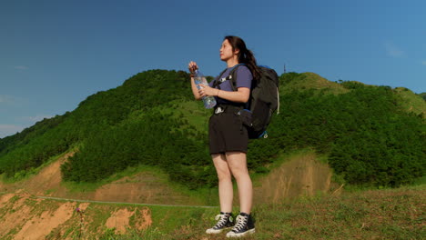 Alleinreisende-Asiatische-Rucksacktouristin-Steht-Auf-Einem-Malerischen-Aussichtspunkt-Auf-Den-Bergen-Und-Trinkt-Mineralwasser-Aus-Einer-Plastikflasche-Nach-Einem-Langen-Wandertag-Auf-Dem-Trekkingpfad