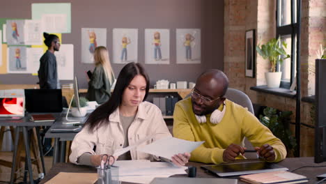 man and woman looking at sketches while sitting at desk in an animation studio