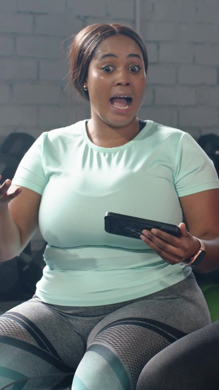 Video verticale: Donna che risponde a un suggerimento di un collega, parlando e gesticolando in palestra con un tablet, indossando un top verde acqua.