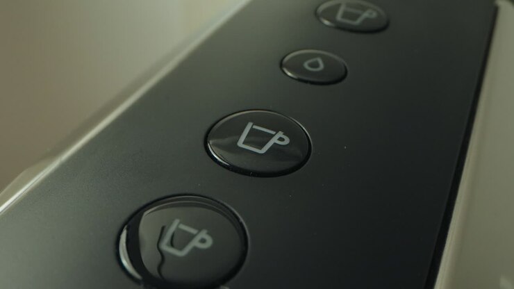 A finger presses a button on a coffee machine to select a drink option