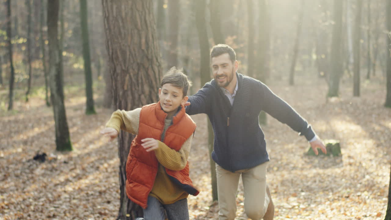 lindo niño pequeño caucásico corriendo en el bosque y su padre siguiéndolo como tratando de atraparlo mientras juegan