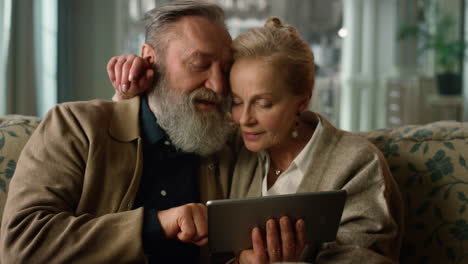 old aged tender couple looking tablet computer together in luxury home