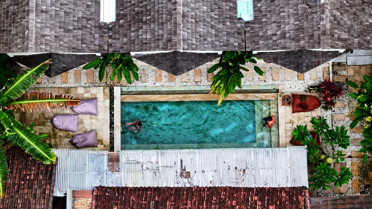 Couple enjoying swimming in a private pool nestled in luxury resort at Bali, captured in top down aerial view