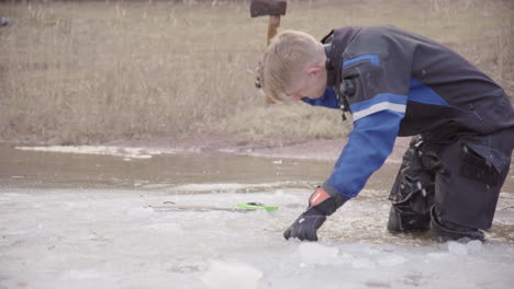 diver in drysuit use axe to smash lake ice to open up entry point for dive