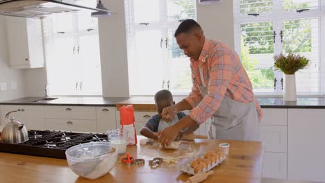 Front-view-of-mid-adult-black-father-and-son-baking-cookies-in-kitchen-of-comfortable-home-4k