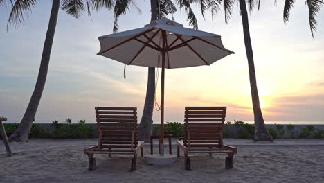 close-up of two empty sun longers under a shade umbrella on the beach facing out toward the setting sun