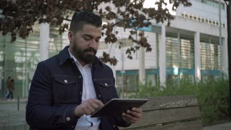Bearded man using digital tablet on street