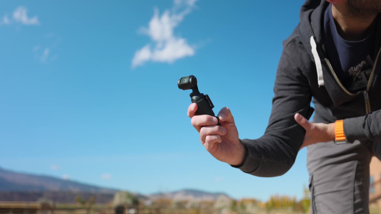 에 손을 들고 있는 혁신적인 dji osmo pocket 3 안정화된 휴대용 카메라와 푸른 하늘을 배경으로