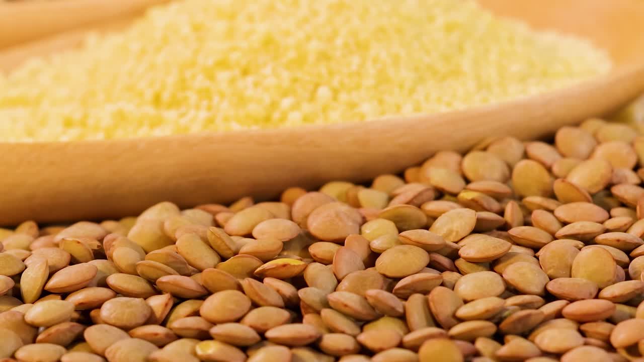 Detailed view of brown lentils and yellow grains on a wooden spoon, showcasing texture and color contrast.