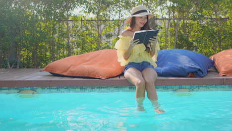 señora asiática en unas vacaciones en solitario leyendo un libro en la piscina