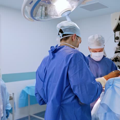 surgery in contemporary operating room. teamwork of surgeons in blue medical uniform performing operation. doctors use microscope during surgery process in clinic.