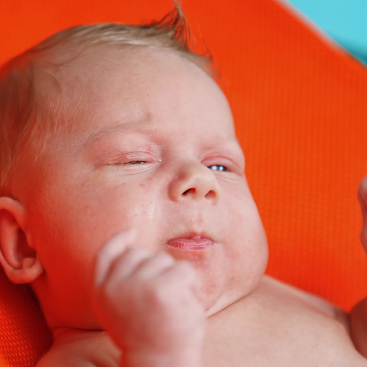 Lovely Caucasian blue-eyed blond infant. Little baby moving hands and making faces. Close up