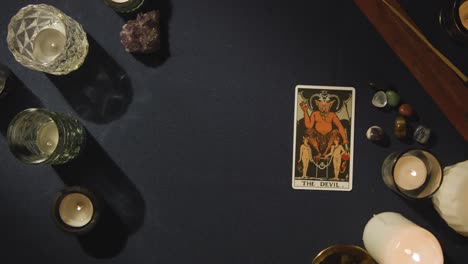 toma aérea de una persona que da una lectura de cartas del tarot colocando la carta del diablo en la mesa 1