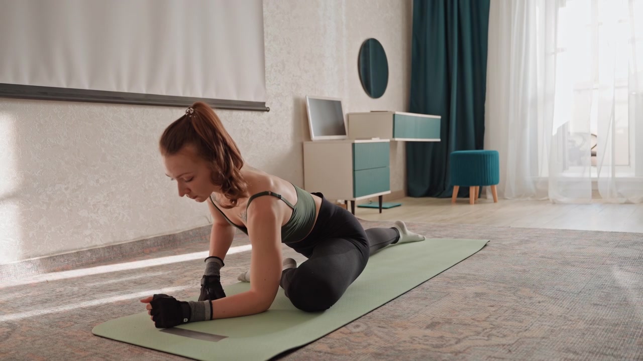 White woman stretching on yoga mat, slow recovery flow in bright bedroom with carpet, gloves and soft sunlight, focused breath work and core engagement, calm atmosphere for post workout mobility