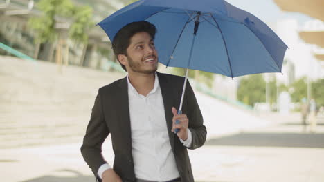 young muslim man opening blue umbrella, hiding from sun.