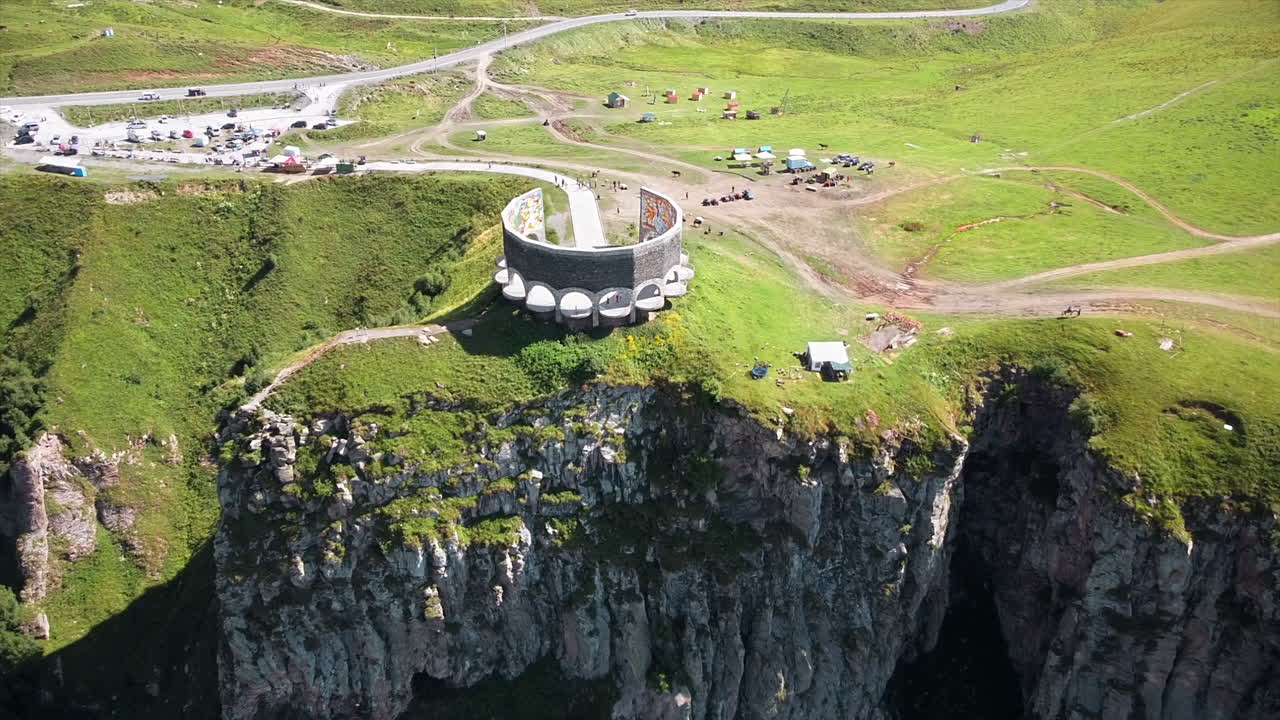 Aerial drone view of a memorial on the edge of a cliff in Caucasus Mountains, Georgia. Greenery, valley, people
