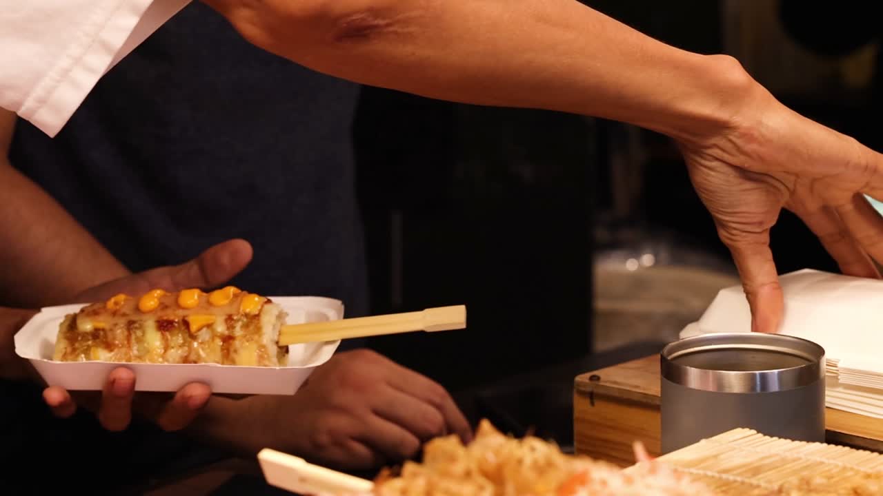 A street vendor carefully places a savory rice roll into a container for a customer
