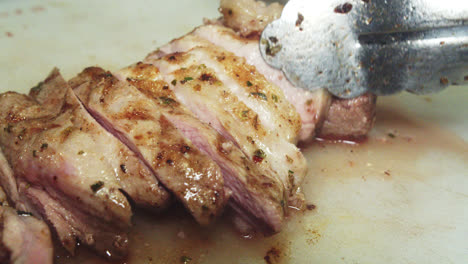 hermoso close-up en cámara lenta de un grupo de pequeños filetes y pedazos recién cortados de lomo de cerdo asado siendo arreglados con pinzas por un chef dentro de una cocina de restaurante