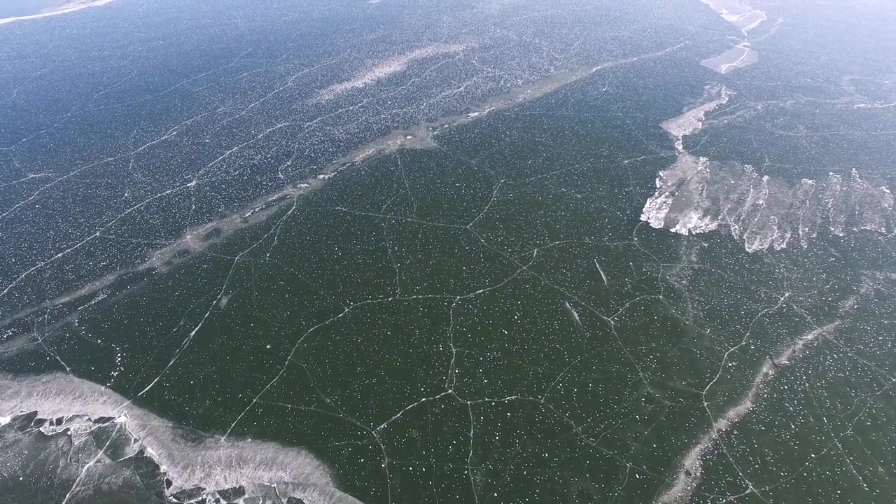 Aerial View of Frozen Lake Surface with Cracks and Open Water