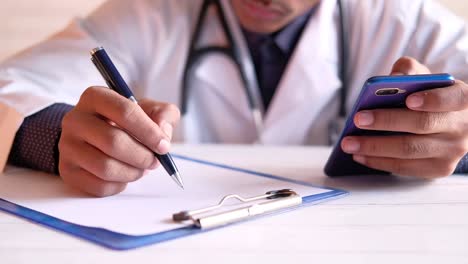 doctor writing notes and consulting on a smartphone