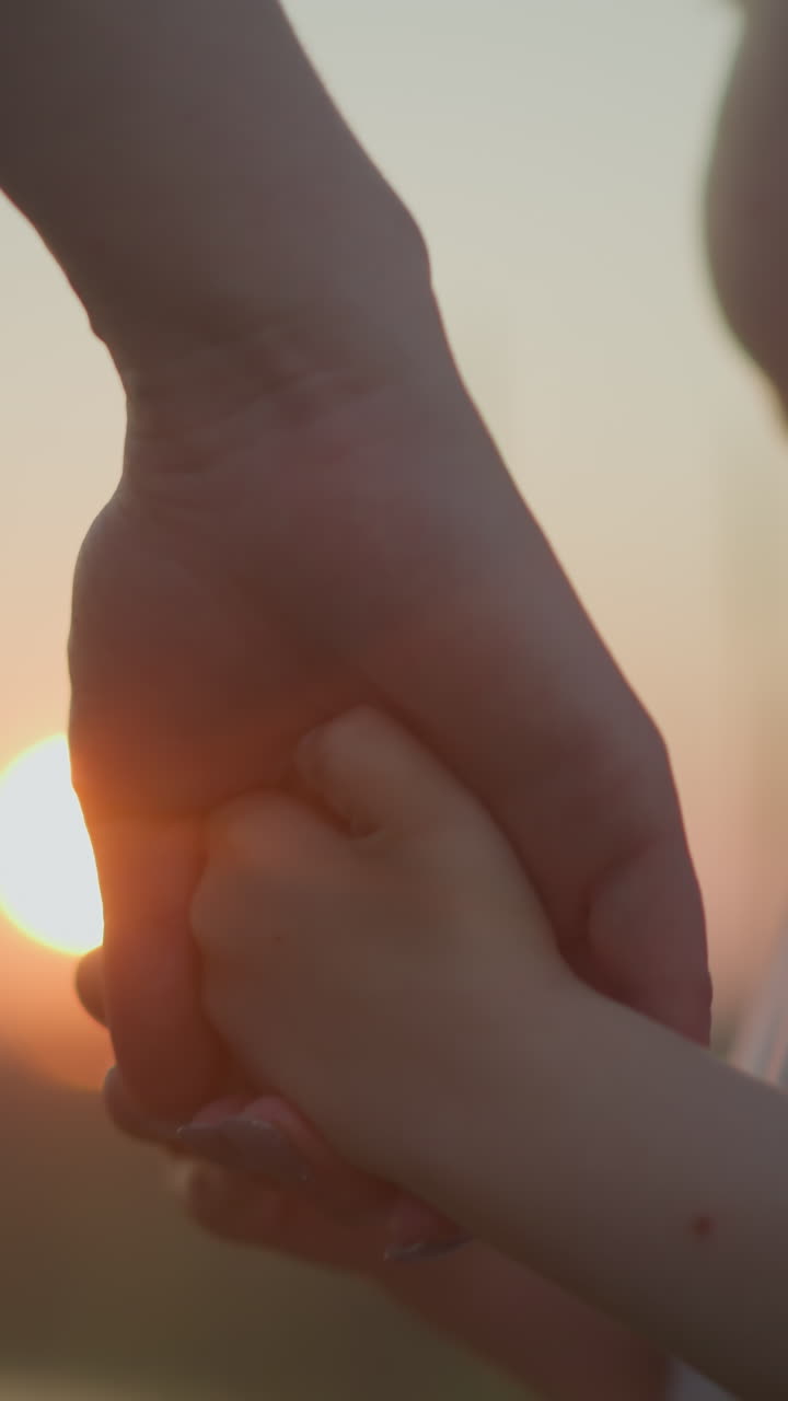 옷을 입은 어린 아들의 손을 들고 함께 서서 조용한 일몰을 지켜보는 어머니의 부드러운 클로즈업 사진.