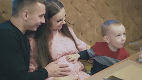 little-boy-puts-hand-on-pregnant-mother-stomach-in-cafe