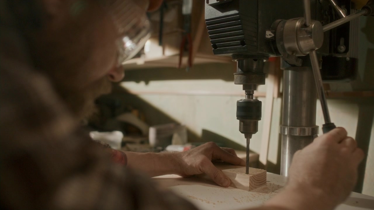 Falegname che pratica un foro in un blocco di legno con una trapano a colonna.