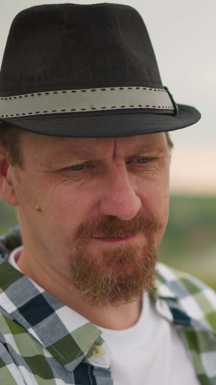 An artist is captured in a moment of deep concentration, his face serious and focused as he works on his painting in a blurry, grassy field. The background fades softly