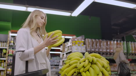 joven hermosa chica morena en sus 20 años recogiendo plátanos y poniéndolos en el carrito de compras en el pasillo de frutas y verduras en una tienda de comestibles