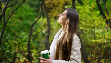 thoughtful calm long-haired lady spending time in the autumn park. woman enjoying the rays of sun coming through the trees. blurred backdrop.