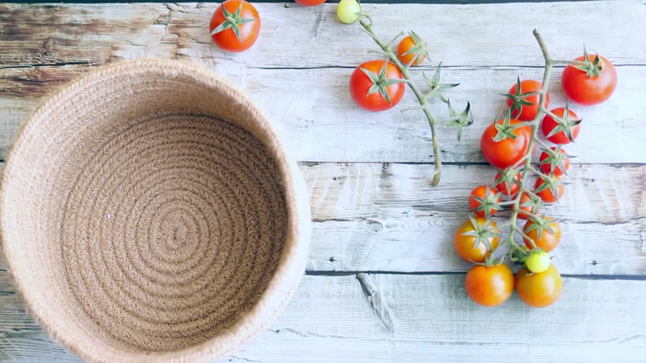 Child's Hand Placing Fresh Tomato into Rustic Basket on Wooden Table