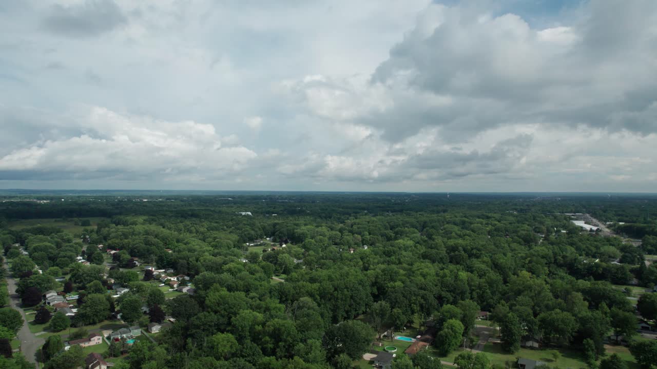 From a great height, a drone captured the small town, which is surrounded by tall trees and a cloudy sky