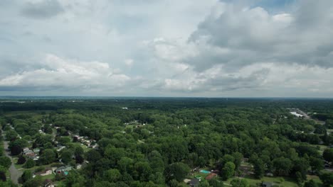 Aus-Großer-Höhe-Erfasste-Eine-Drohne-Die-Kleine-Stadt,-Die-Von-Hohen-Bäumen-Und-Einem-Wolkigen-Himmel-Umgeben-Ist