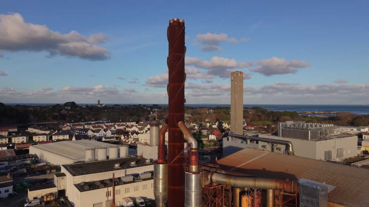 St Sampson Guernsey panorerende droneoptagelse af kraftværkskompleks og skorstene i gylden sol med interessant himmel og hav i baggrunden.