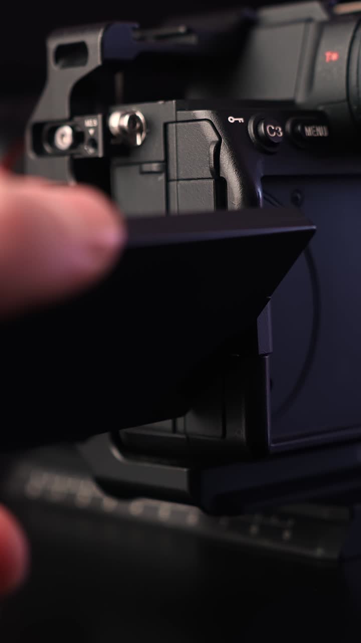 Una mano gira e ruota il display LCD articolato sul corpo di una fotocamera mirrorless, primo piano di un'attrezzatura da vlogging e del flusso di lavoro del creatore. Verticale