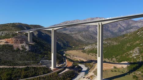 aerial shot of the fully finished moracica bridge in montenegro. the big red coat of arms of montenegro is seen on one of the bridge's pillar