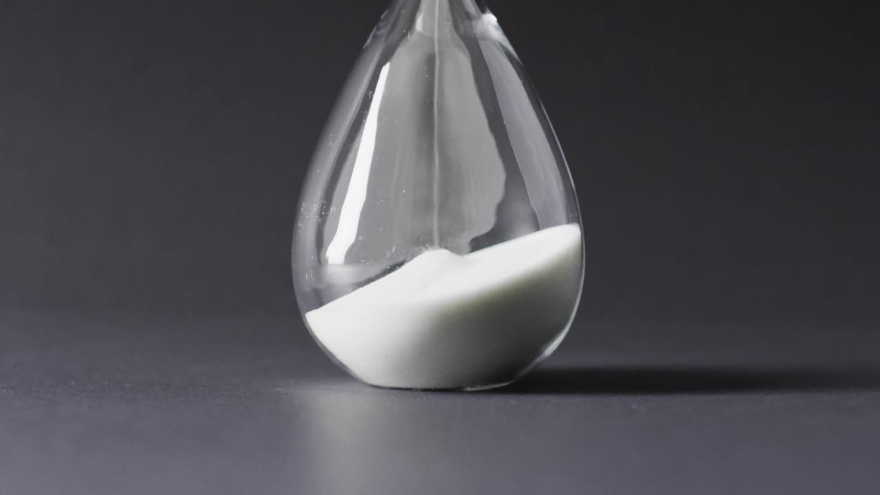 Video of close up of hourglass with sand pouring, copy space on black background