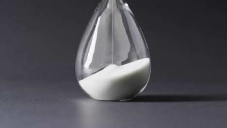 Video-of-close-up-of-hourglass-with-sand-pouring,-copy-space-on-black-background