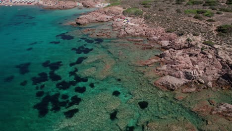 tomada aérea lateral de la costa rocosa y la gente nadando en la isla de maddalena, cerdeña, italia