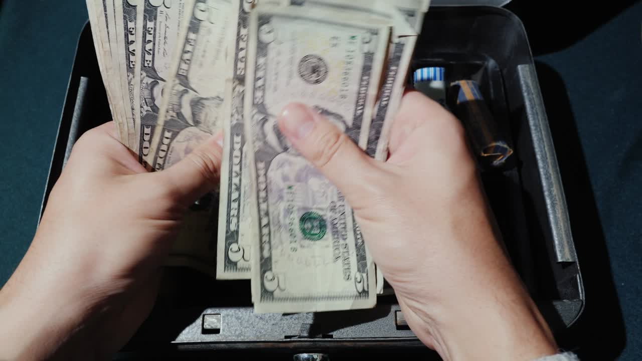 Kassereren teller opp pengene i amerikanske dollar. På bakgrunn av en bærbar pengeboks