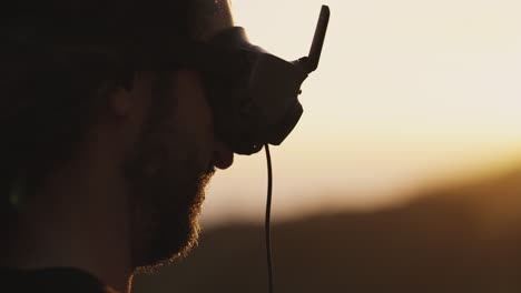 Man-with-beard-and-long-hair-puts-on-goggles-for-FPV-drone,-close-up
