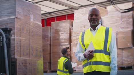 portrait of mature male freight haulage manager in high vis by lorry being loaded with boxes